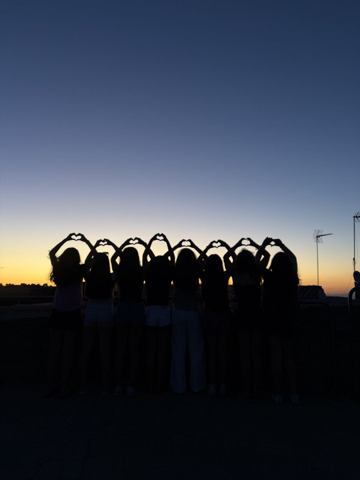 Les alumnes fan cors amb les mans a contrallum de la posta de sol